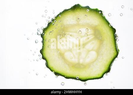 Cetriolo affettato con bolle d'acqua su sfondo bianco. Concetto di cosmetici idratanti per la pelle. Sano dissetante detox cetriolo acqua. Foto Stock