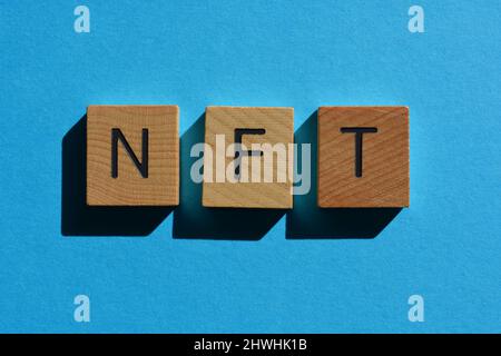 NFT, abbreviazione di token non-fungibile, in lettere in legno su sfondo blu Foto Stock