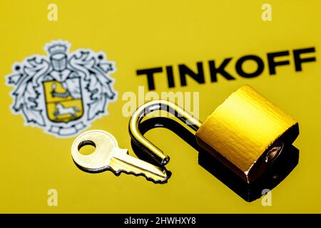 Un lucchetto di sicurezza aperto e chiave sullo sfondo del logo della banca Tinkoff in riflessione speculare Foto Stock