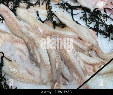 Primo piano di molti filetti di pesce fresco di merluzzo bianco atlantico crudo su ghiaccio al banco nel supermercato Foto Stock