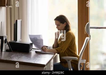 La donna seria si siede alla scrivania tiene i fogli che rivedono l'infografica Foto Stock