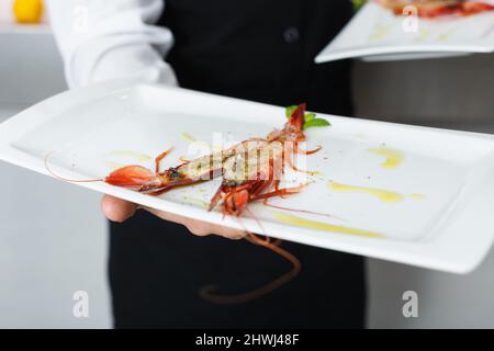 Langoustina alla griglia su piatto in mano al cameriere Foto Stock