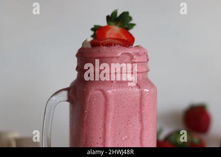 Frullato a base di fragole fresche, banana e latte di mandorle. Servito in vasetto di mason. Girato su sfondo bianco con banane e fragole intorno. Foto Stock