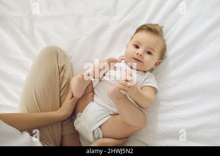 Felice, sano, adorabile bambino o ragazza che indossa un pannolino sul letto con la madre Foto Stock