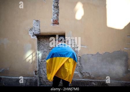 Protestante coperto di bandiera Ucraina blu e gialla che protestano contro la guerra in Ucraina per strada Foto Stock