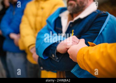 Sparato di manifestanti con nastri e bandiere ucraini blu e gialli che protestano contro la guerra in Ucraina per strada Foto Stock