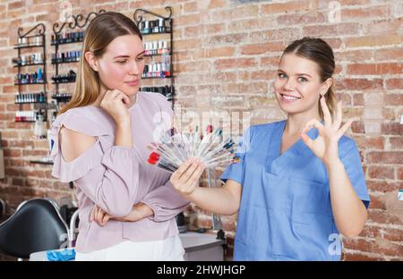 Ragazza che sceglie il colore di smalto del chiodo con il manicurist nel salone del chiodo Foto Stock