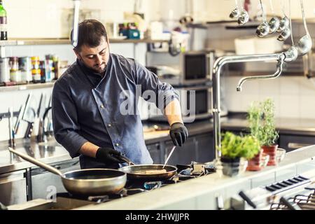 Lo chef professionista cucina nel ristorante su due padelle. Foto Stock
