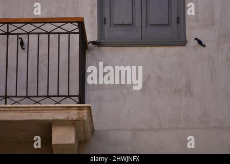 Facciata neoclassica con persiane in legno grigio e un balcone con ringhiera artigianale in ferro battuto contro una parete rosa in stucco in Grecia. Foto Stock