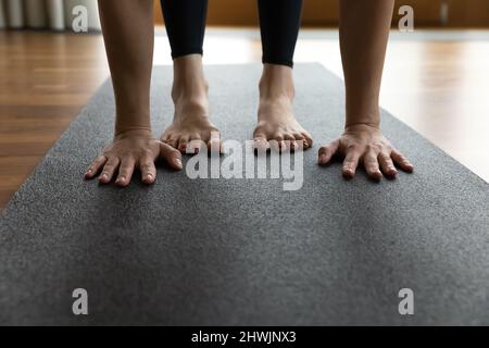 Donna in piedi su tappeto esegue Utttanasana, palmi e piedi primo piano Foto Stock