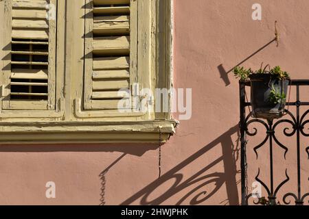 Antica facciata neoclassica con una parete in stucco veneziano, una finestra con persiane in legno intemperato e un balcone con ringhiera in ferro battuto in Grecia. Foto Stock