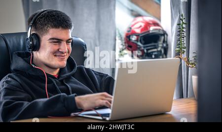 Un giovane atleta maschio si siede di fronte a un computer portatile nella sua stanza. Foto Stock