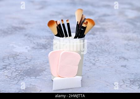 closeup il mazzo bianco marrone makeup kit spazzola con spugne palla nella scatola di plastica su sfondo grigio marrone fuori fuoco. Foto Stock