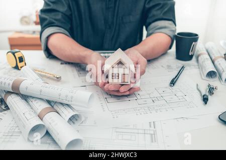 Architetto ingegnere mani tenere e proteggere mini casa modello su bueprint. Proteggere Casa, progettazione di pianificazione dei costi e concetto di costruzione. Foto Stock