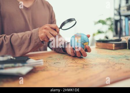 Un uomo usa lente d'ingrandimento vedere Globe sfera orb modello vintage stile. Concetto di viaggio, avventura e scoperta. Foto Stock