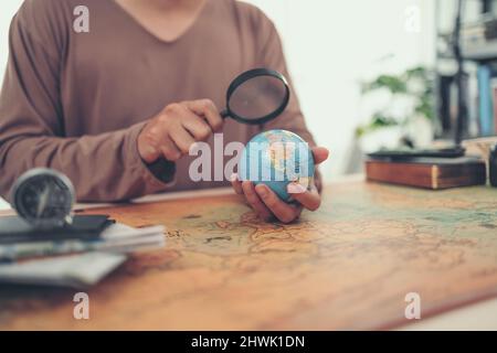 Un uomo usa lente d'ingrandimento vedere Globe sfera orb modello vintage stile. Concetto di viaggio, avventura e scoperta. Foto Stock