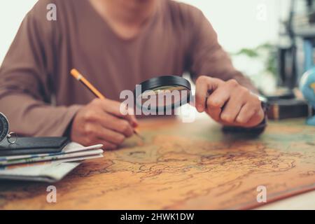 Un uomo usa lente d'ingrandimento e la mano che scrive il controllo sulla mappa del mondo. Concetto di viaggio, avventura e scoperta. Foto Stock