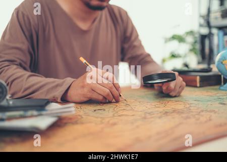 Un uomo usa lente d'ingrandimento e la mano che scrive il controllo sulla mappa del mondo. Concetto di viaggio, avventura e scoperta. Foto Stock