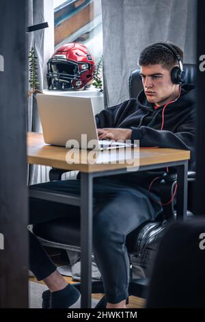 Un giovane atleta maschio si siede di fronte a un computer portatile nella sua stanza. Foto Stock