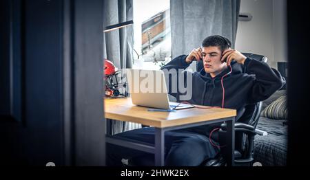 Un giovane atleta maschio si siede di fronte a un computer portatile nella sua stanza. Foto Stock