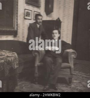 fotografia d'epoca di due fratelli seduti in salotto uno di loro sul braccio del divano e l'altro sulla poltrona. Hanno molti dipinti su di loro. erano forse collezionisti d'arte o mecenati la cui opera d'arte in loro dolce casa. periodo: foto originale originale degli anni '1910. ULTERIORI-DIRITTI-CLEARANCE-INFO-NOT-AVAILABLE / collezionista d'arte e casa Foto Stock