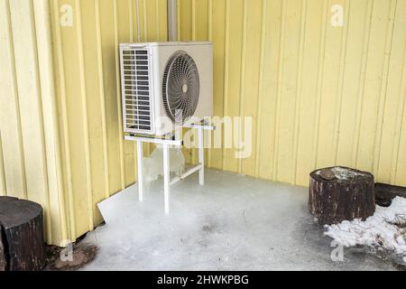 Aria condizionata macchina all'aperto su rack casa domestica parete gialla. Molto ghiaccio sotto di esso in freddo giorno d'inverno. Foto Stock