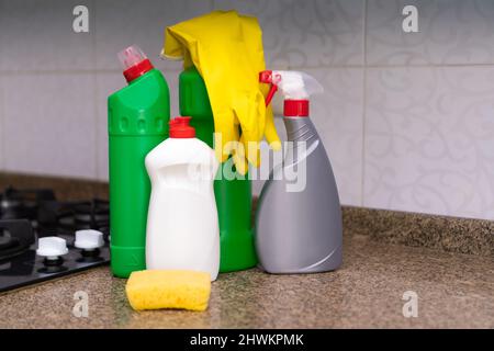 Primo piano di prodotti per la pulizia, guanti di gomma gialli, una spugna sul tavolo da cucina vicino alla stufa a gas. Concetto di pulizia, lavori domestici Foto Stock