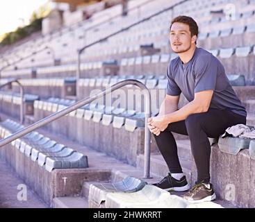 Tutto in un'unica cosa. Scatto di un bel giovane uomo seduto in piedi in un'arena di atletica. Foto Stock
