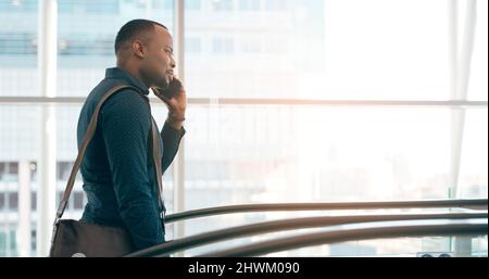 Su chiamata e in viaggio. Scatto corto di un bel giovane uomo d'affari che prende una telefonata mentre salendo una scala mobile in un ambiente di lavoro moderno. Foto Stock