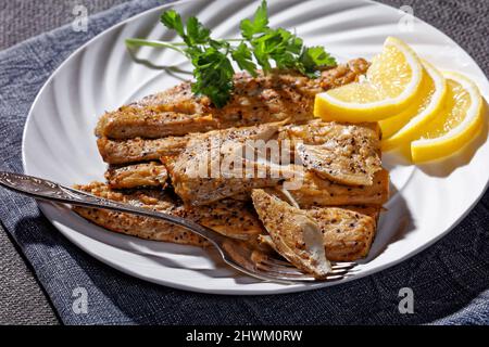 filetti di sgombro piccanti su un piatto bianco con fette di limone e forchetta Foto Stock