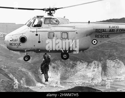 Winchman Norman Harris e il Coastguard Bob Newsome sono stati sollevati in un elicottero RAF Westland vorticoso HAR10 mentre si alza sulle scogliere a Flamborough. L'aeromobile e l'equipaggio hanno partecipato a un esercizio seguito dal Vice Marshal Air C V Winn, AOC 18 Maritime Group. 1st marzo 1973 Foto Stock