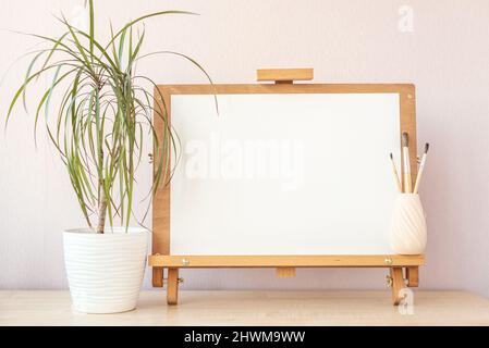 Carta bianca bianca bianca per la pittura su cavalletto di legno sul tavolo dello studio di casa Foto Stock