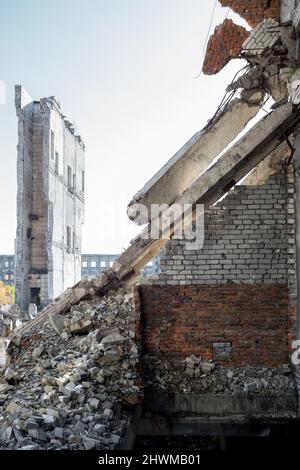 Un muro di mattoni in rovina con appesi pezzi di sostegno sullo sfondo dei resti di un edificio distrutto. Sfondo. Foto Stock