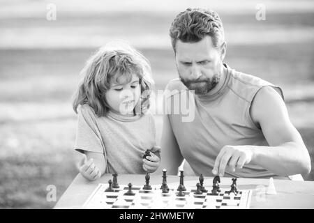 Figlio che si stesa sull'erba e gioca a scacchi con il padre. Ragazzo concentrato sviluppare strategia di scacchi, giocando gioco da tavolo con il genitore. Giochi e. Foto Stock