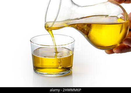 Olio extravergine di oliva versato dal decanter in una tazza di vetro su sfondo bianco Foto Stock