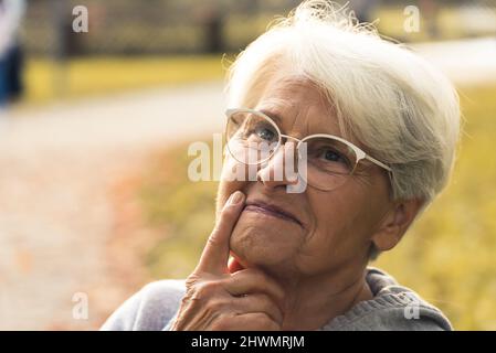 Donna caucasica dai capelli grigi con occhiali sul naso, toccandola al viso e pensando a qualcosa. Foto di alta qualità Foto Stock