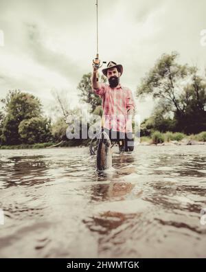 Uomo pesca e relax mentre si gode l'hobby. Pesca felice pescatore in fiume tenendo canne da pesca. Trota iridea Steelhead. Trota marrone essere Foto Stock