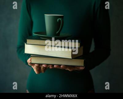 Ragazza in verde tenendo pochi libri e una tazza di caffè Foto Stock