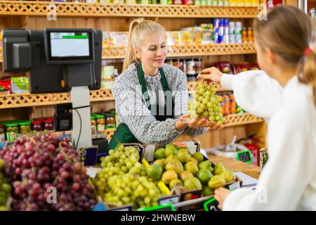 Donna venditore che prende le uve da donna acquirente per pesare Foto Stock