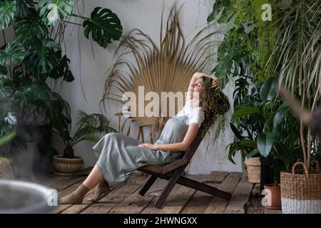 Soddisfatto calmo donna fiorista rilassarsi in giardino interno godere di equilibrio mentale e benessere a casa Foto Stock