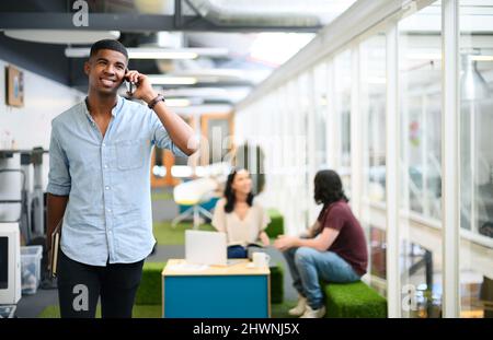 SA certamente come camminare e parlare. Scatto di un giovane uomo d'affari che parla su un cellulare mentre cammina attraverso un ufficio. Foto Stock