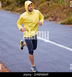 Tutto il tempo, tutto l'impegno di superficie. Scatto ad angolo alto di un bel giovane uomo che corre in condizioni di pioggia. Foto Stock