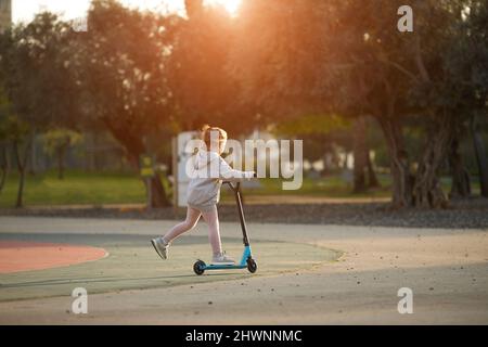 Piccola bella ragazza guida uno scooter nel parco Foto Stock