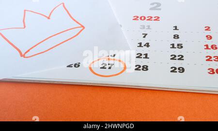 Primo piano di un calendario cartaceo il 27 aprile 2022 con sfondo arancione e corona disegnata a mano nei colori tradizionali della celebratio del Re Foto Stock