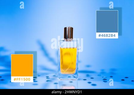 Bottiglia di profumo dorata in vetro su sfondo blu acciaio con ombre di piante. Campioni di colori 4682B4 e FFA500. Modello colori con cosmetici. Foto Stock