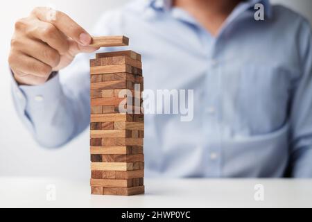 Uomo d'affari che posiziona o tira il blocco di legno sulla torre. Pianificazione aziendale, gestione dei rischi, concetti relativi a soluzioni e strategie Foto Stock