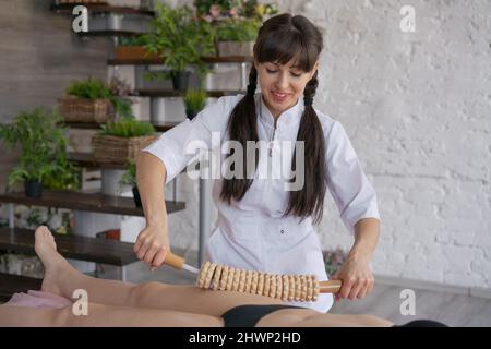 Primo piano sulla schiena donna non identificata con massaggio anticellulite sessione con terapia madero, terapista professionista che tiene attrezzi in legno in studio o salone con spazio copia Foto Stock