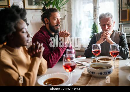 Famiglia e concetto religioso. Gruppo di persone multietniche con cibo che prega prima del pasto Foto Stock