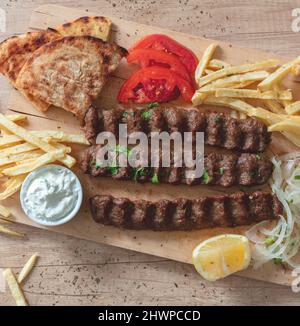 Shish kebab, doner souvlaki, arrostito di carne tradizionale Street food. Piatto etnico, pita pane, tzatziki yogurt patate e cipolla su tavola di legno, vista dall'alto Foto Stock