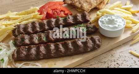 Shish kebab, doner souvlaki, arrostito di carne tradizionale Street food. Piatto etnico, pita pane, tzatziki yogurt patate e cipolla su tavola di legno, primo piano Foto Stock